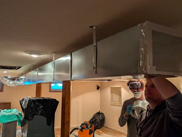 Two Henry Brothers technicians hanging sheet metal trunk ductwork in Jeffersonville Indiana basement