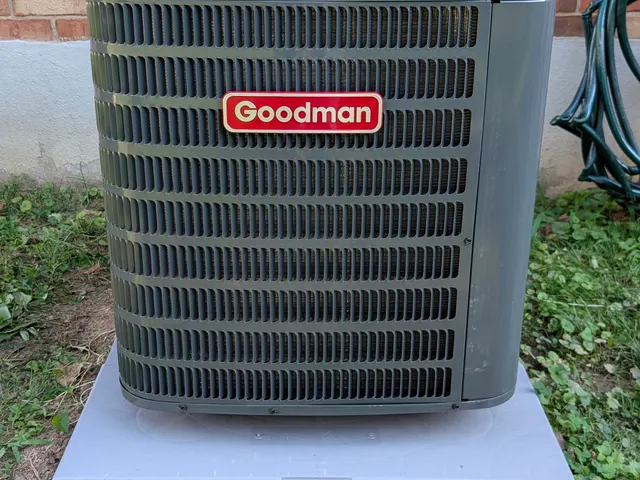 Goodman central AC condenser installed on its pad outside a brick home