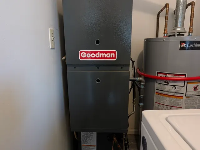 Goodman gas furnace installed in a utility closet with new supply plenum and green inspection tag attached