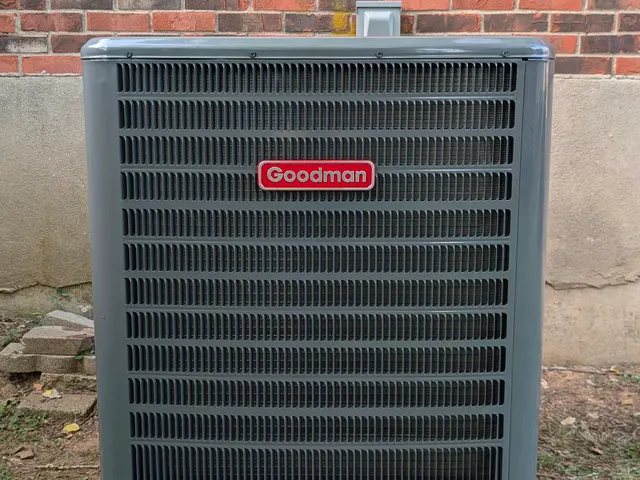 Goodman AC condenser against a brick exterior wall after HVAC service, front view