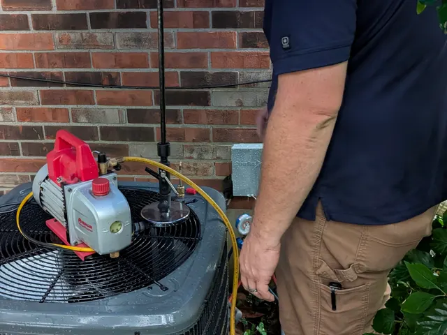 Henry Brothers technician pulling a vacuum on a new Goodman AC condenser with a vacuum pump under an umbrella in the rain, Jeffersonville Indiana