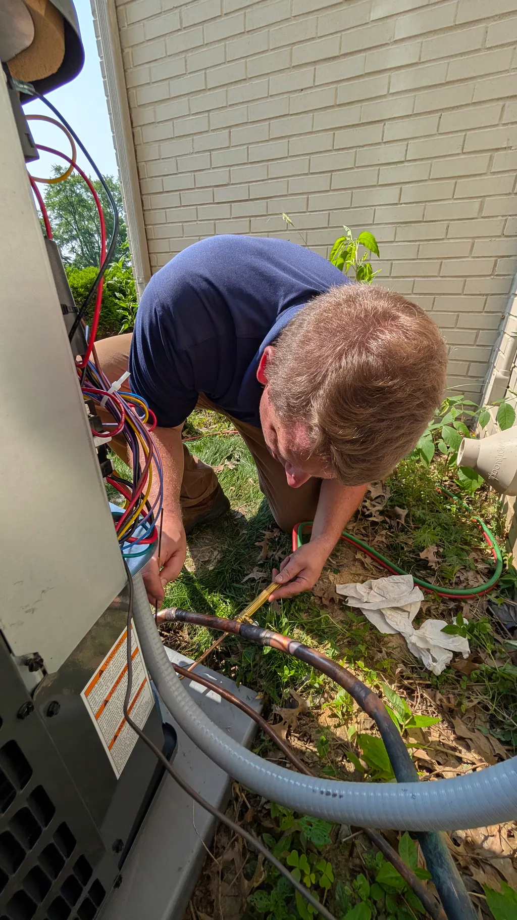 Henry Brothers technician brazing the copper refrigerant line at an outdoor condenser in New Albany, Indiana