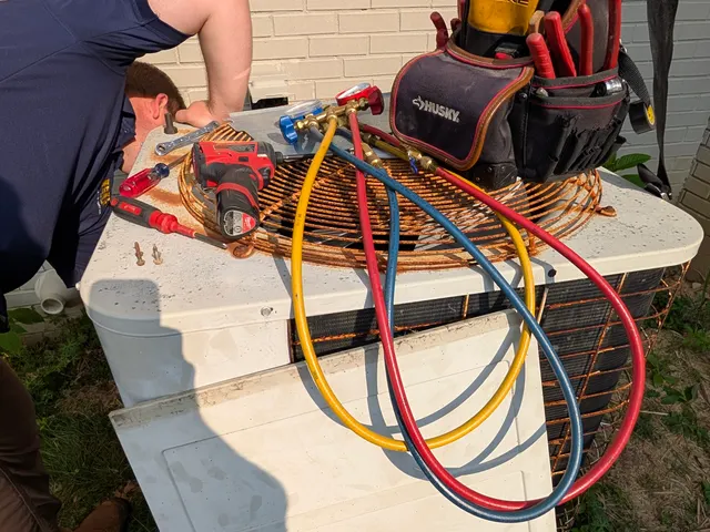 Henry Brothers technician servicing older central AC condenser unit with manifold gauges in New Albany Indiana