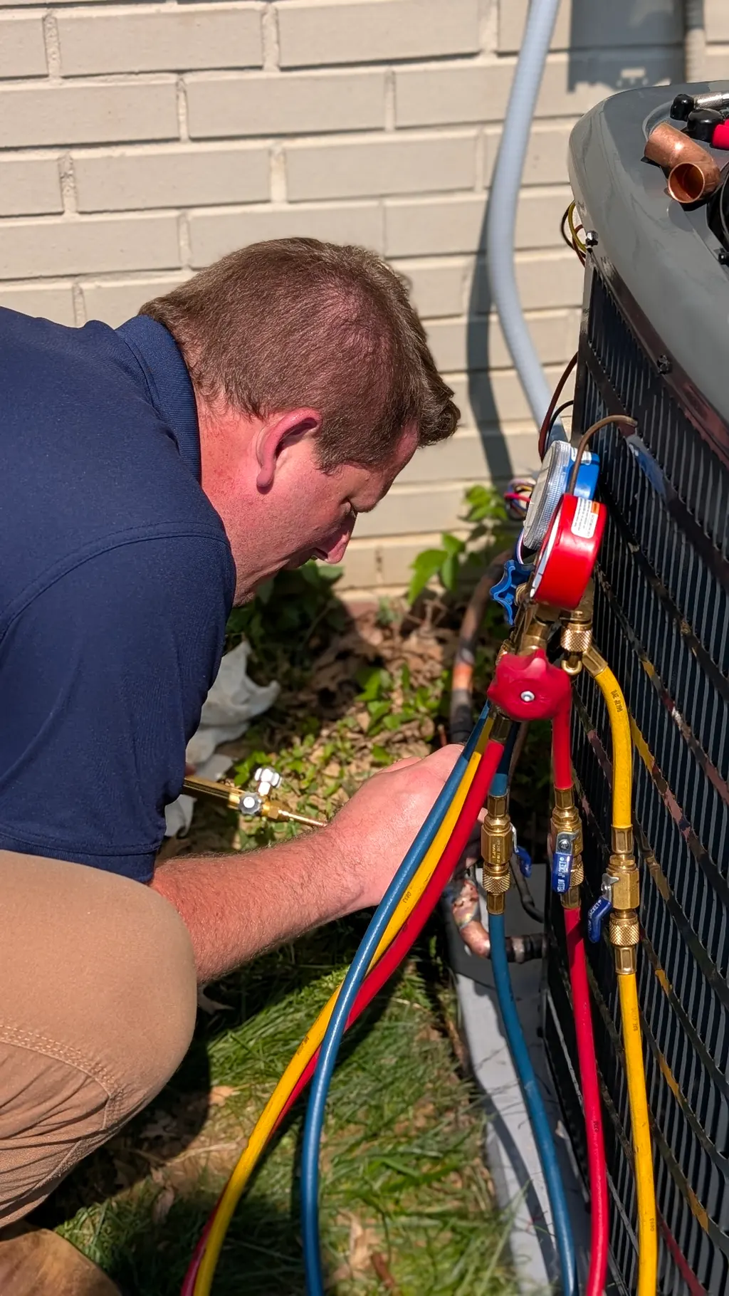 Henry Brothers technician reading refrigerant manifold gauges on outdoor AC condenser unit New Albany Indiana