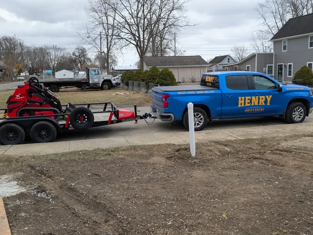 Henry Brothers branded blue Silverado with equipment trailer and compact track loader parked at a job site