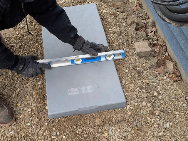 Technician using a level to check the condenser mounting pad sits flat before the outdoor unit goes on