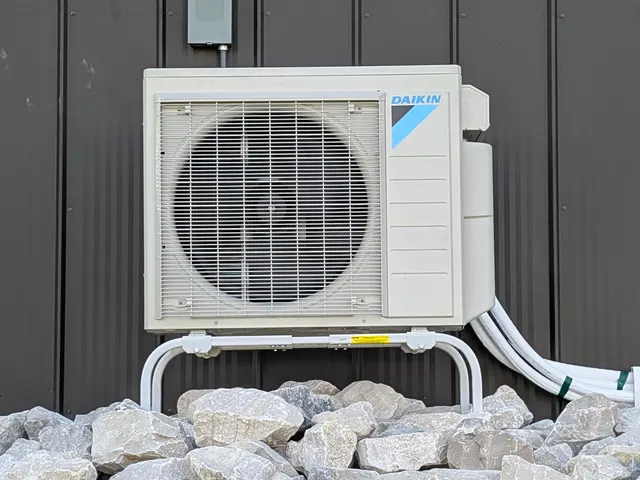 Completed Daikin mini-split outdoor condenser unit mounted on brackets beside dark metal barn Indiana