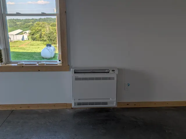 Completed Daikin floor-console mini-split install inside pole barn with sunny Indiana farmland through window