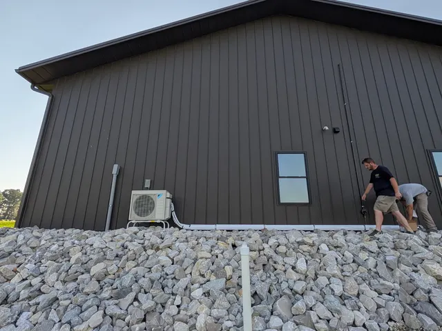 Henry Brothers crew finishing a Daikin mini-split install on a large dark metal pole barn in rural Southern Indiana