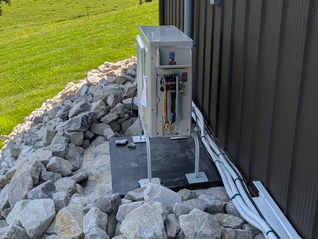 Daikin mini-split condenser mid-install on rock bed beside dark metal pole barn Indiana