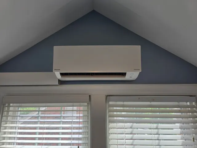 Daikin mini split indoor unit mounted on the gable wall above two windows under a vaulted ceiling in southern Indiana