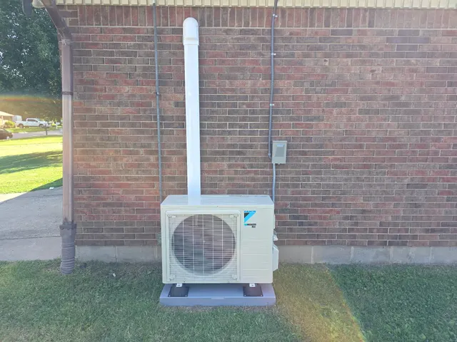 Completed Daikin mini-split outdoor condenser unit installed on pad beside brick home exterior