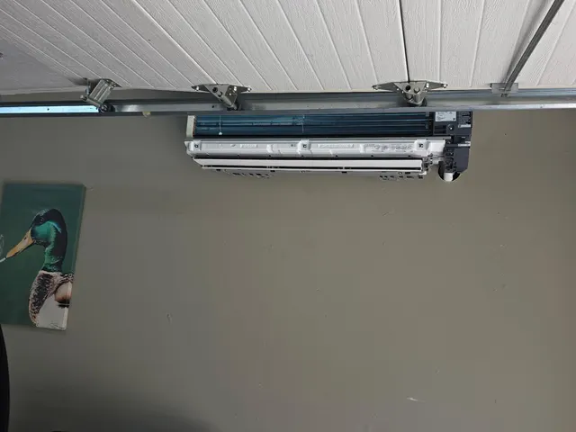 Ductless mini split indoor head with its front housing off, mounted on a garage wall below the garage door track