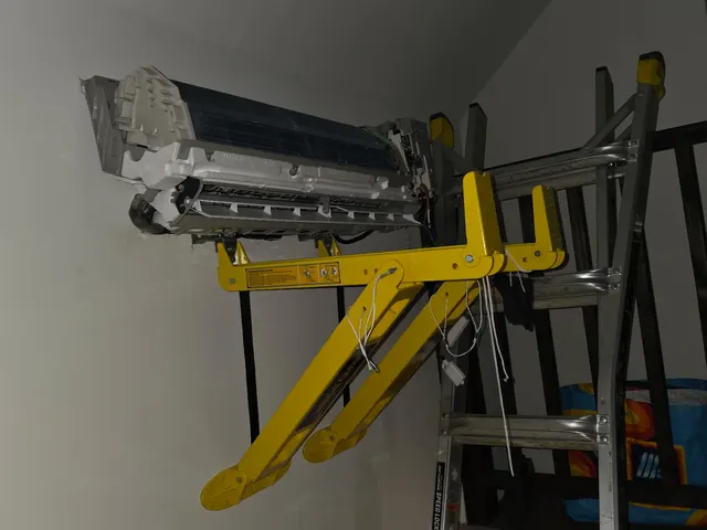 Mini-split indoor head unit suspended on wall lift bracket during high-wall installation process