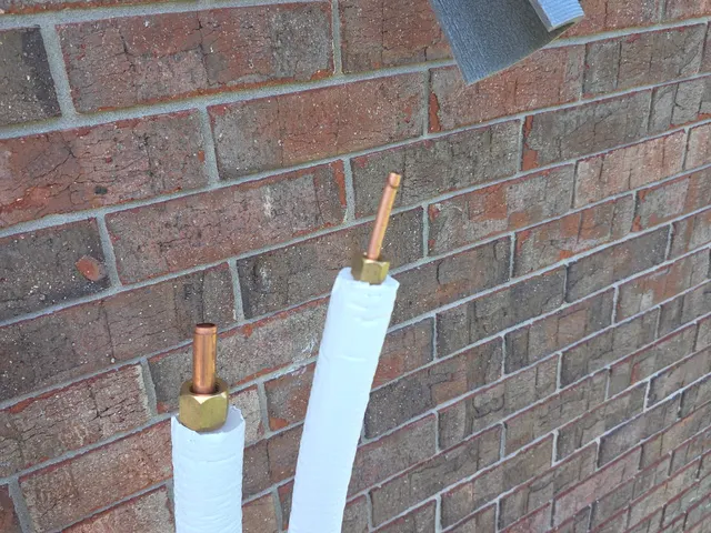 Insulated copper refrigerant line set pipes staged against brick wall before mini-split connection