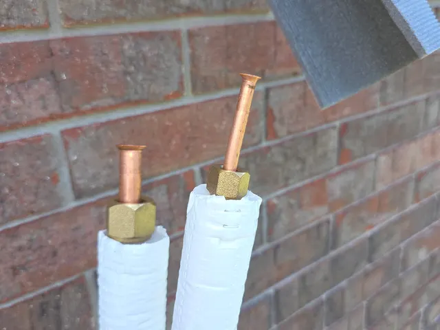 Pair of insulated mini-split refrigerant copper lines with brass flare nuts at brick exterior