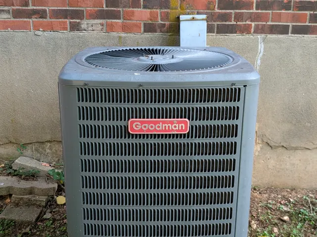 Goodman central AC condenser against a brick exterior wall before an HVAC inspection