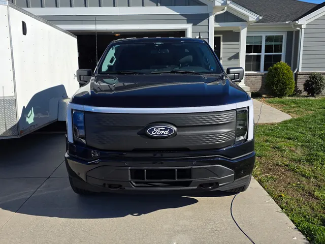 Ford F-150 Lightning electric service truck charging on the driveway at the Henry Brothers home base, work trailer parked behind